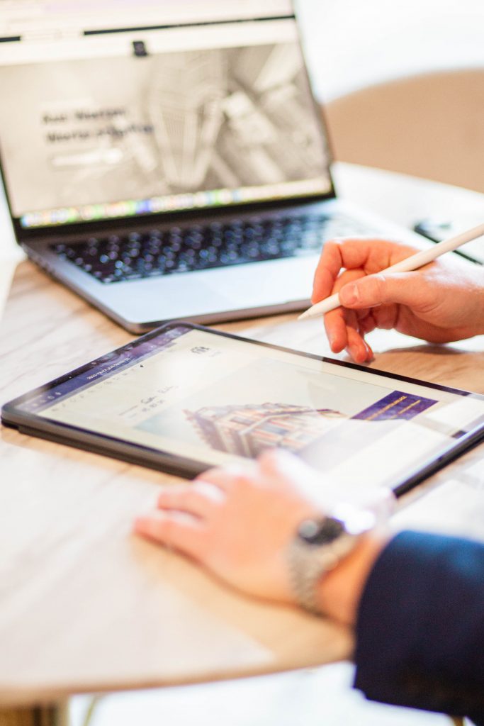 Ein Mitarbeiter sitzt am Schreibtisch und führt eine Beratung am Tablet durch, während im Hintergrund ein Laptop zu sehen ist.